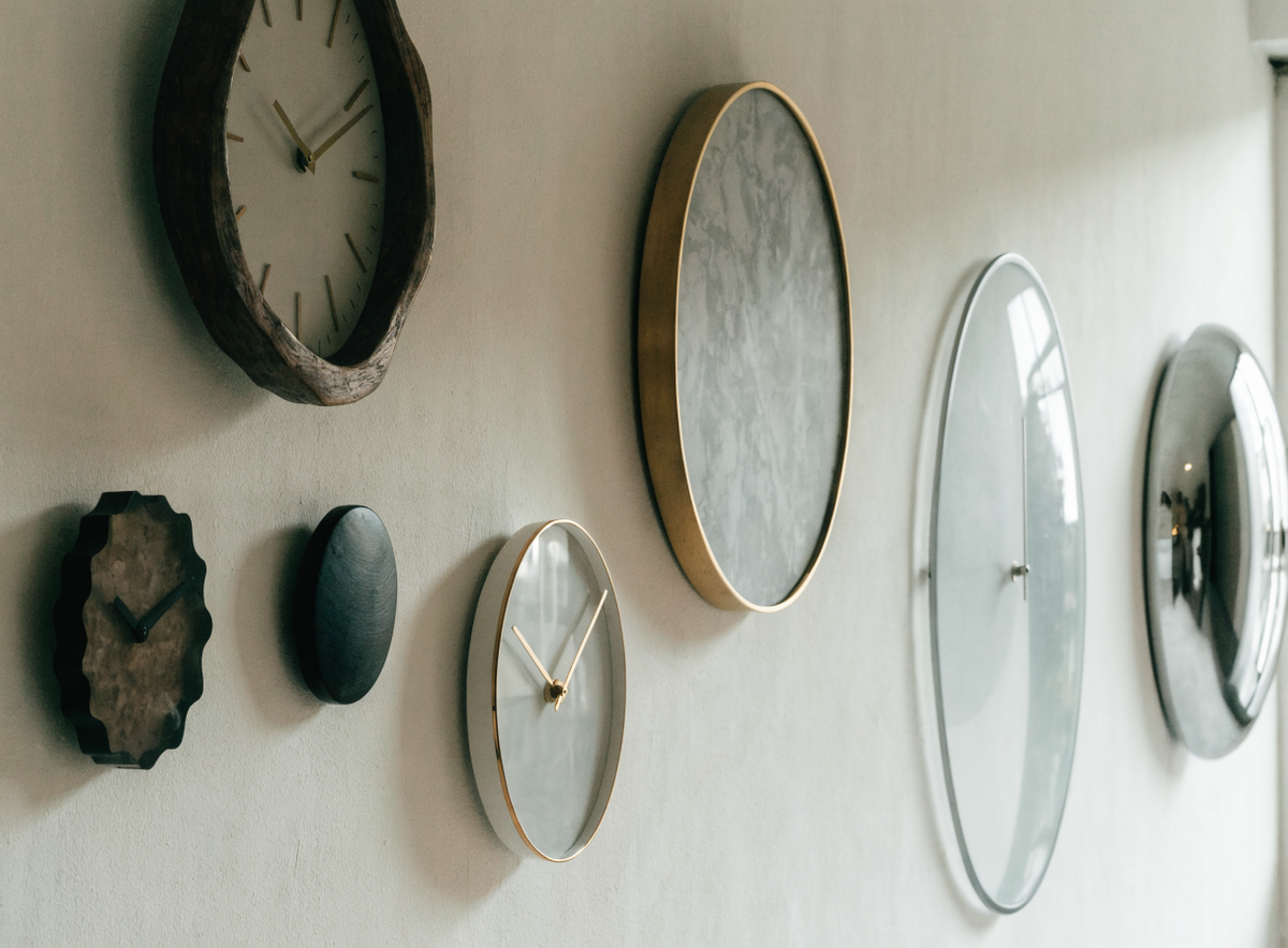 Plusieurs horloges murales de tailles et styles différents sur un mur clair Image
